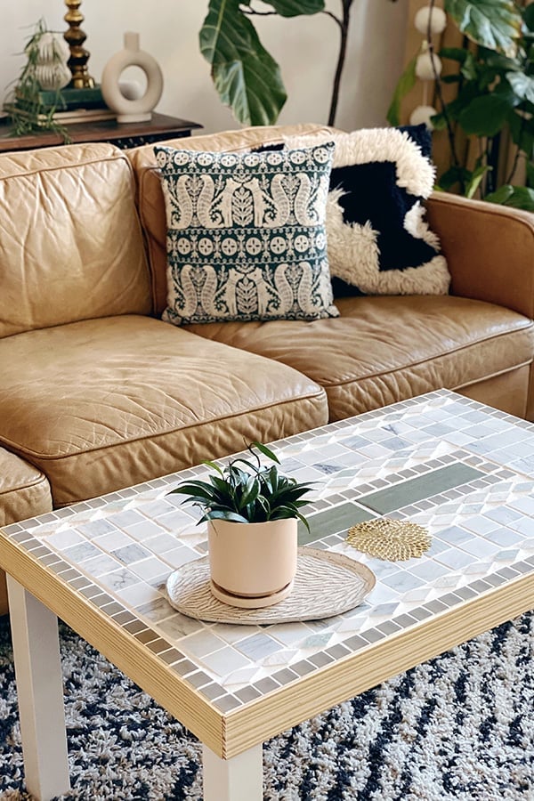 IKEA hack coffee table with a white and green mosaic tile top and a potted plant in front of a tan leather sofa with pillows