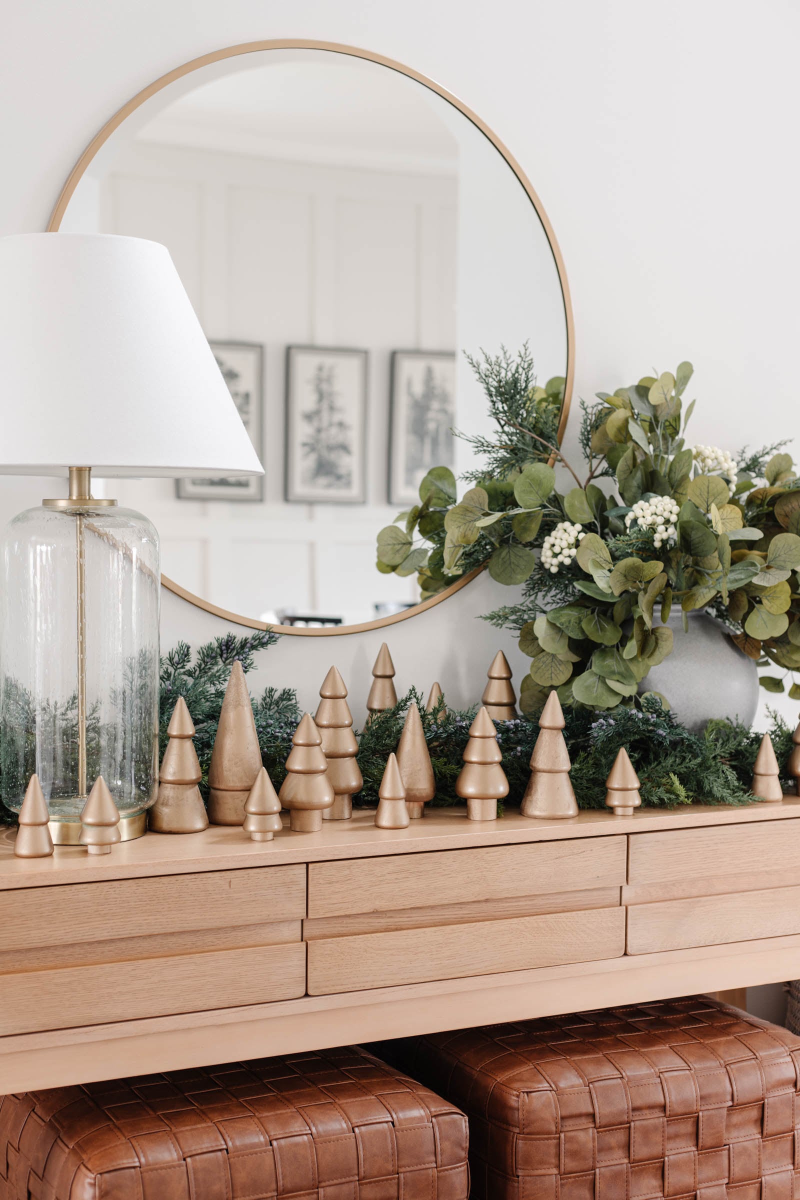 Gold spray painted wooden Christmas trees in many sizes lined along a light wood console with cedar and eucalyptus greenery
