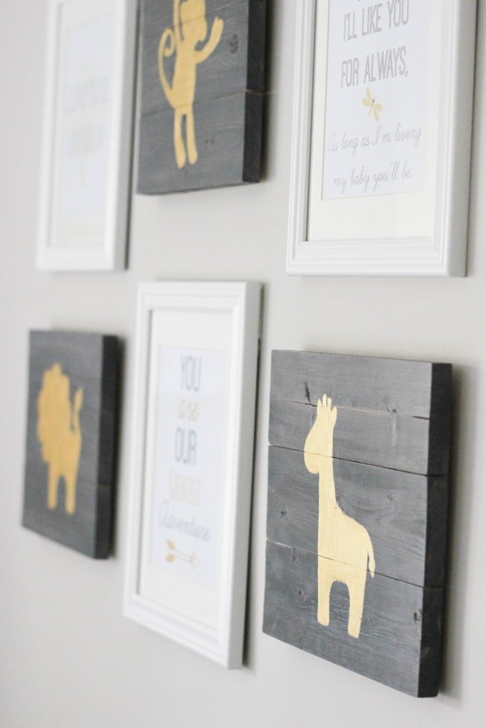 Gallery wall of gray stained wood panels painted with gold monkey, lion and giraffe silhouettes between white framed quotes