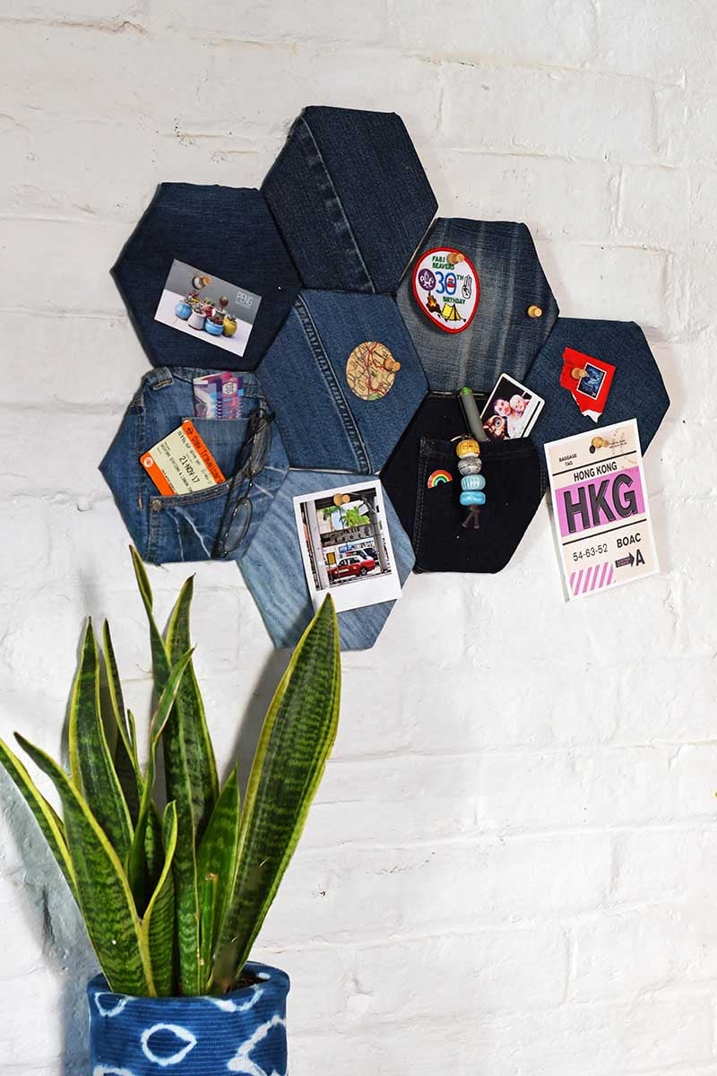 Hexagon denim pin board in mixed blue washes with jeans pockets, pinned badges and travel tickets on a white brick wall