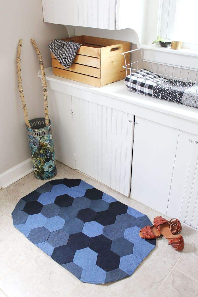 Hexagon patchwork denim rug in light, medium and dark blue shades on a laundry room floor beside sandals and a basket