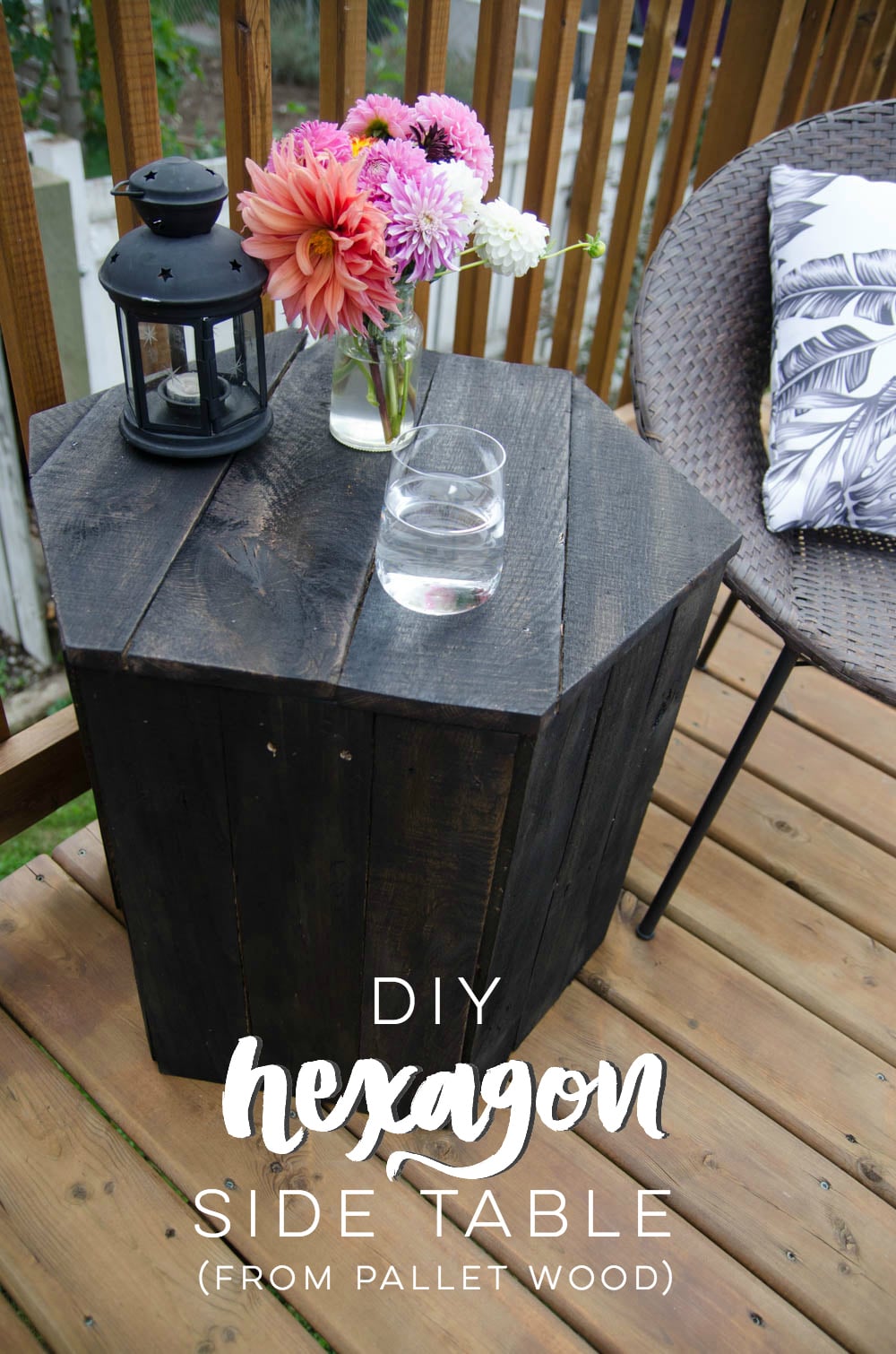 Dark stained hexagon pallet wood side table between two wicker chairs on a deck, topped with dahlias and a black lantern