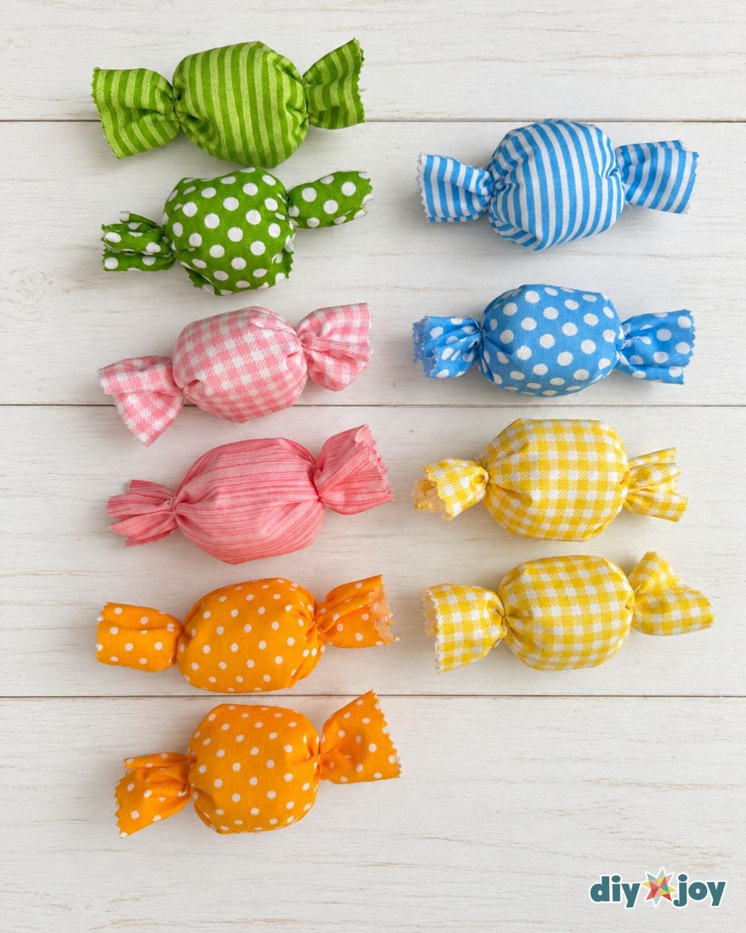 Eleven finished no-sew fabric candies in green, blue, pink, yellow and orange prints lined up on white wood planks