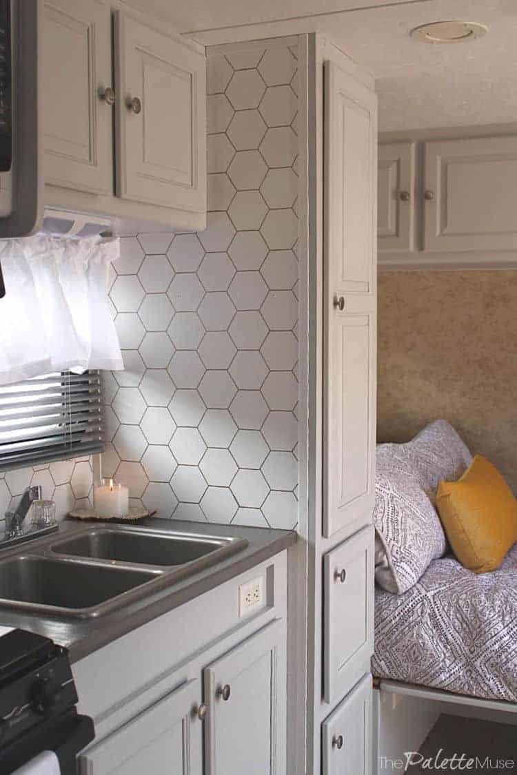 Camper kitchen with light gray painted laminate cabinets, a stainless sink and a white hexagon tile backsplash