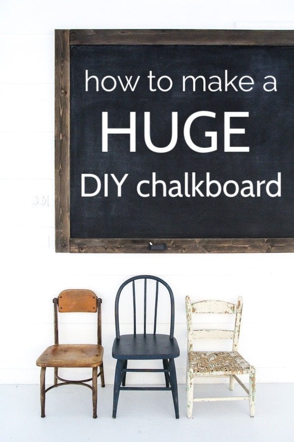 Huge dark wood framed chalkboard about eight feet wide on a white wall above three mismatched vintage wooden kids chairs