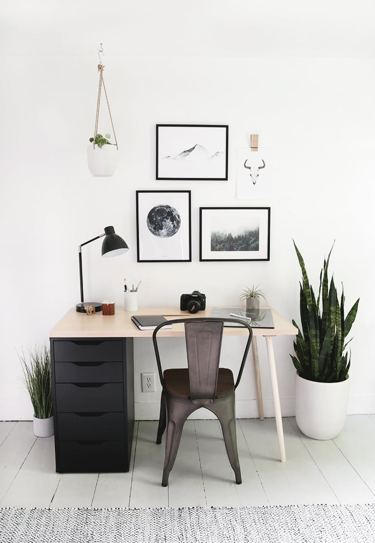 Modern desk with black IKEA Alex drawer unit, light wood top and dowel leg, metal chair and black framed prints above
