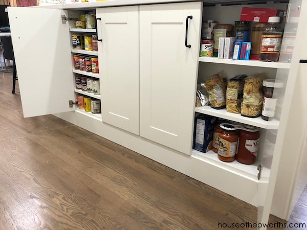 Kitchen island with white shaker doors open to shallow shelves of canned goods, jars and pasta boxes