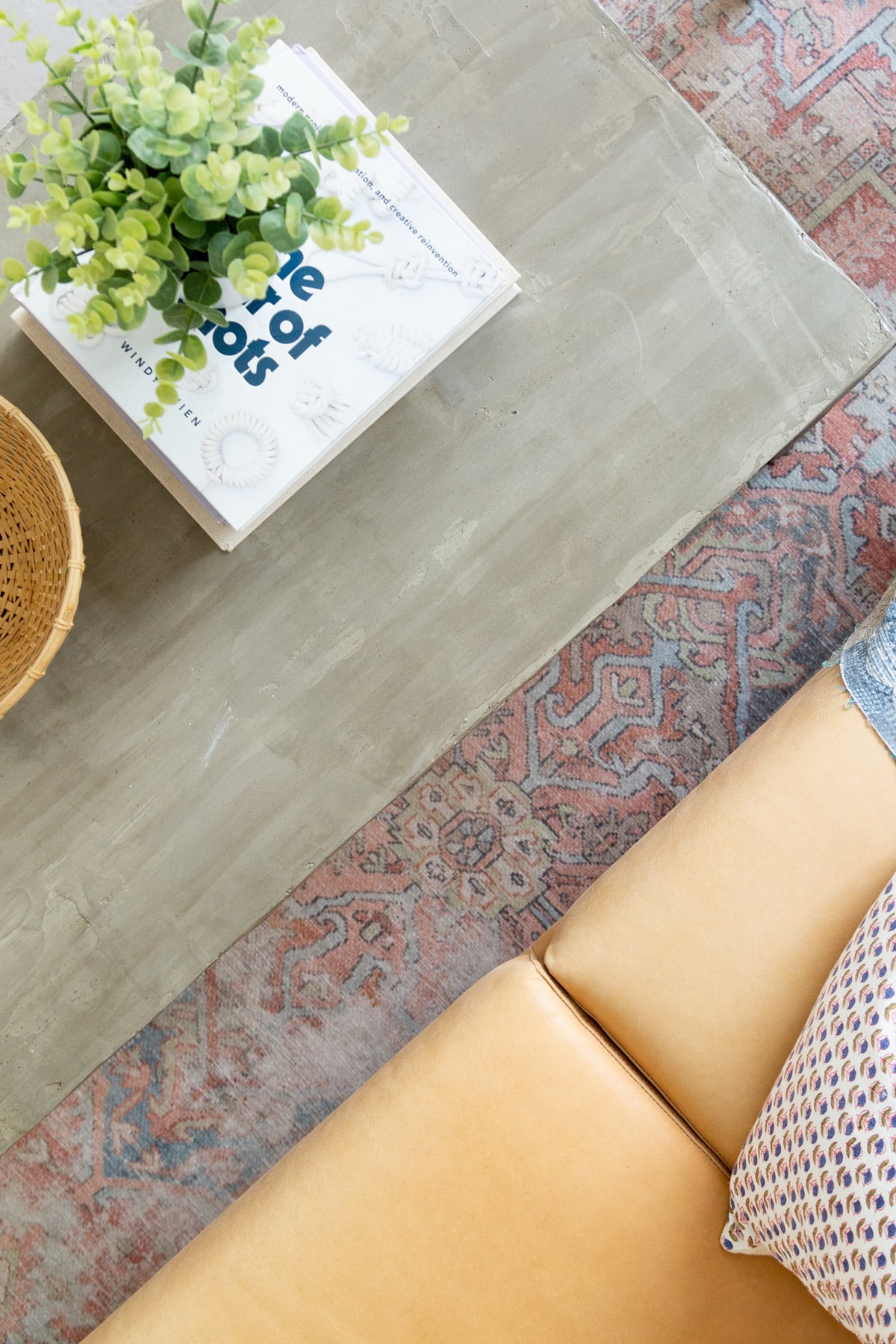 IKEA Hack Concrete Coffee Table | Feather Finish DIY Close view of a smooth gray concrete finished coffee table top with a book, a small plant and a tan leather sofa