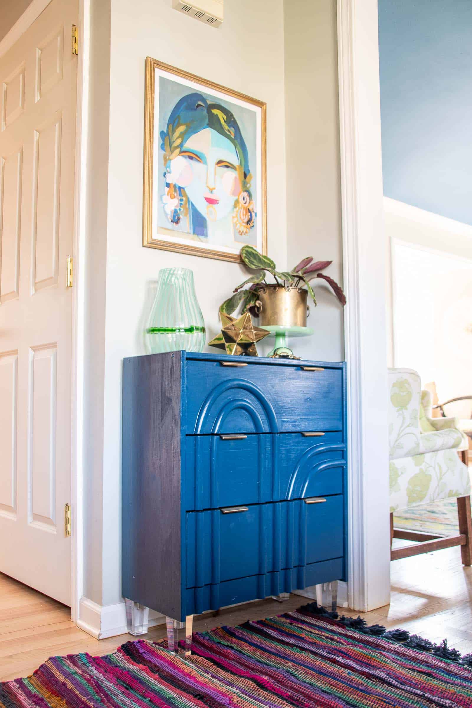 IKEA Rast Dresser Mid-Century Makeover | IKEA Bedroom Hack Blue high gloss IKEA Rast dresser with arched trim across three drawers, brass pulls and clear acrylic legs on a striped rug