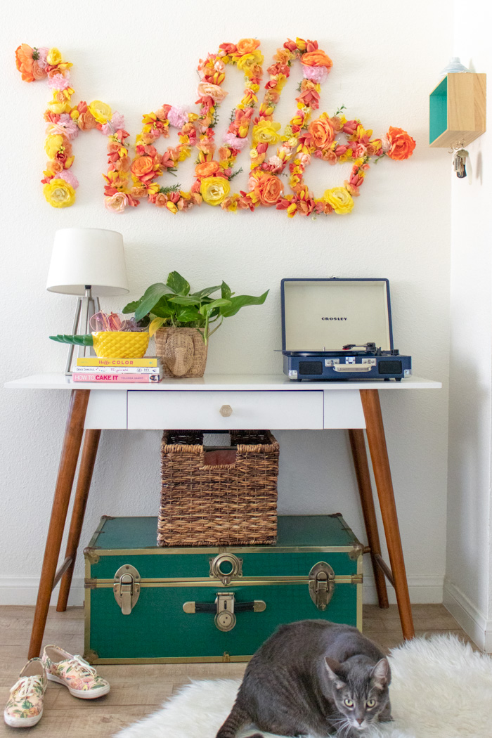Large floral word art spelling hello in cursive covered with pink, white and yellow faux flowers in an entryway
