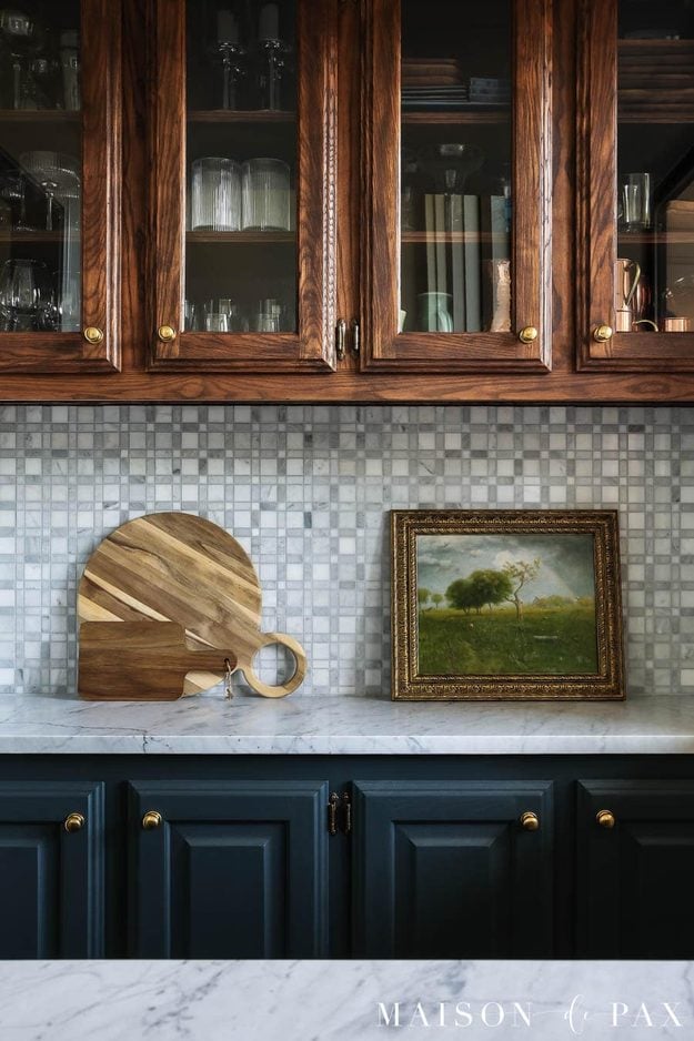 Marble Mosaic Bar Backsplash | Adhesive Mat Install Gray and white marble mosaic backsplash between dark wood glass-front cabinets and navy lowers, with a cutting board
