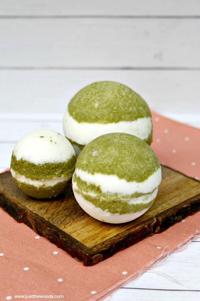 Three green and white layered homemade matcha vanilla bath bombs sitting on a wooden board over a soft pink cloth napkin