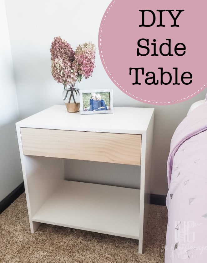 White plywood side table with a natural wood drawer front and an open lower shelf, topped with dried hydrangeas and a photo