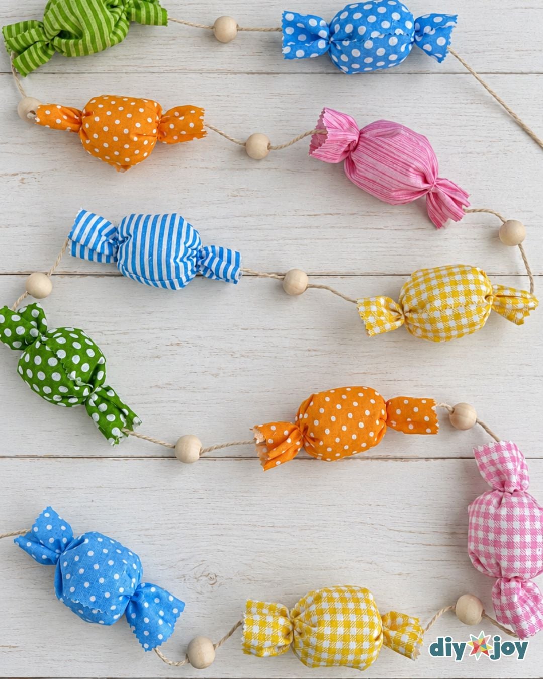 Finished DIY candy garland with polka dot, striped and gingham fabric candies spaced by wooden beads on white wood
