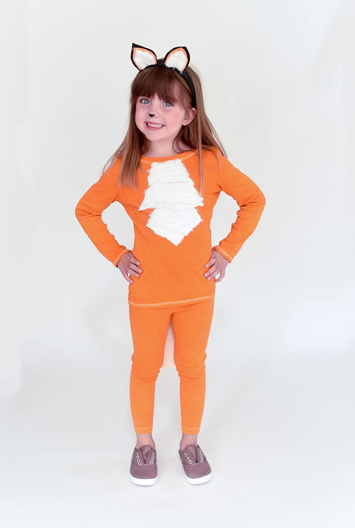 Smiling girl in an orange tee and leggings with a white faux fur chest patch, felt fox ears headband and painted fox nose