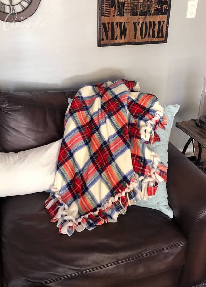 Red, blue and white plaid no-sew fleece blanket with a pulled-through edge draped over a dark brown leather sofa