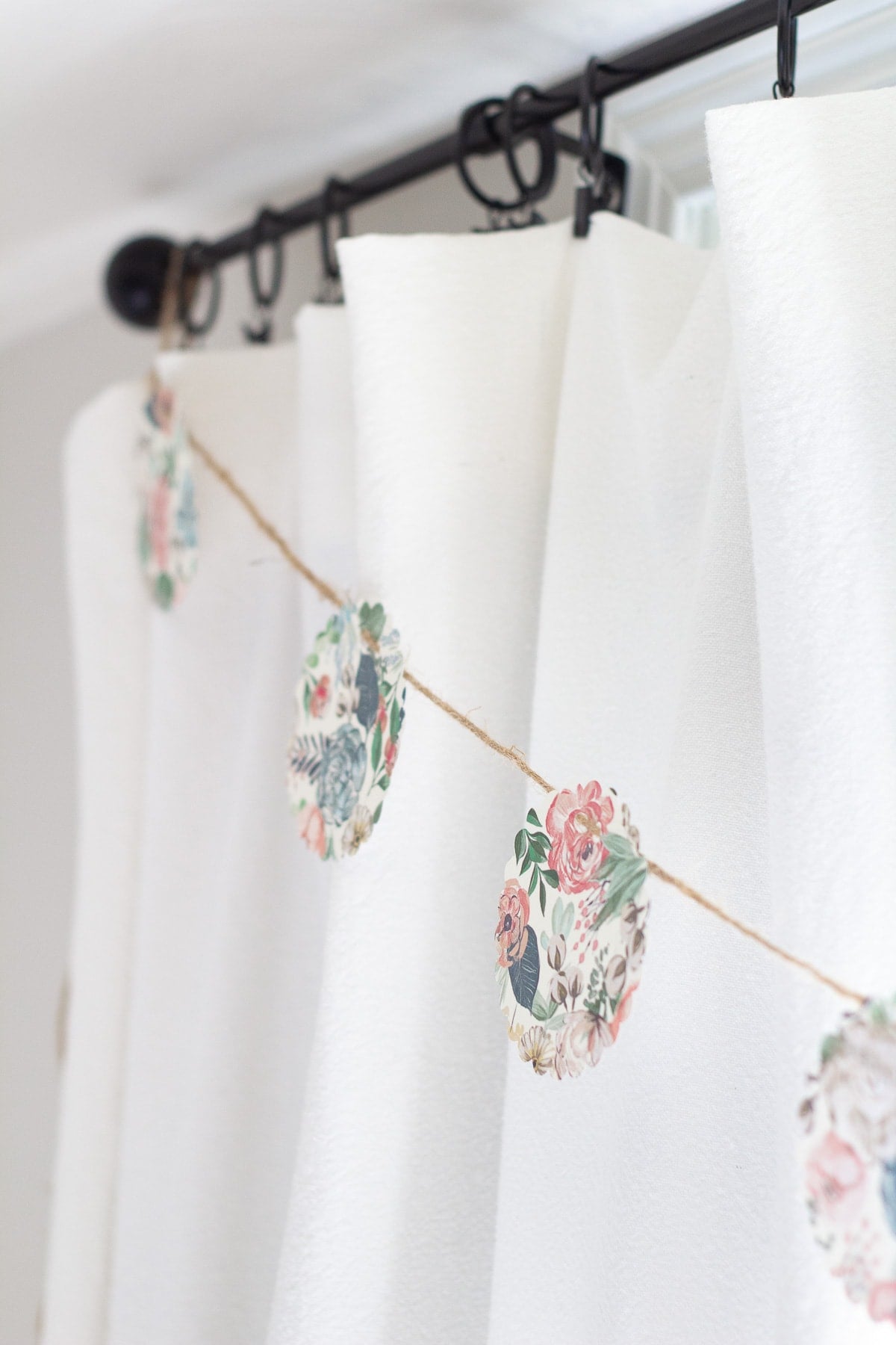 No-Sew Paper Circle Garland | DIY Party Decorations Idea Paper garland of floral scalloped circles strung on twine across white curtains hanging from a black curtain rod