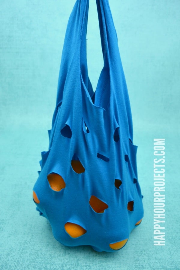 Blue t-shirt mesh produce bag with staggered cut holes and oranges inside, hanging against a turquoise background