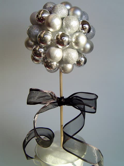 Silver ornament ball topiary on a wood dowel with a black sheer ribbon bow and long trailing tails in a white pot