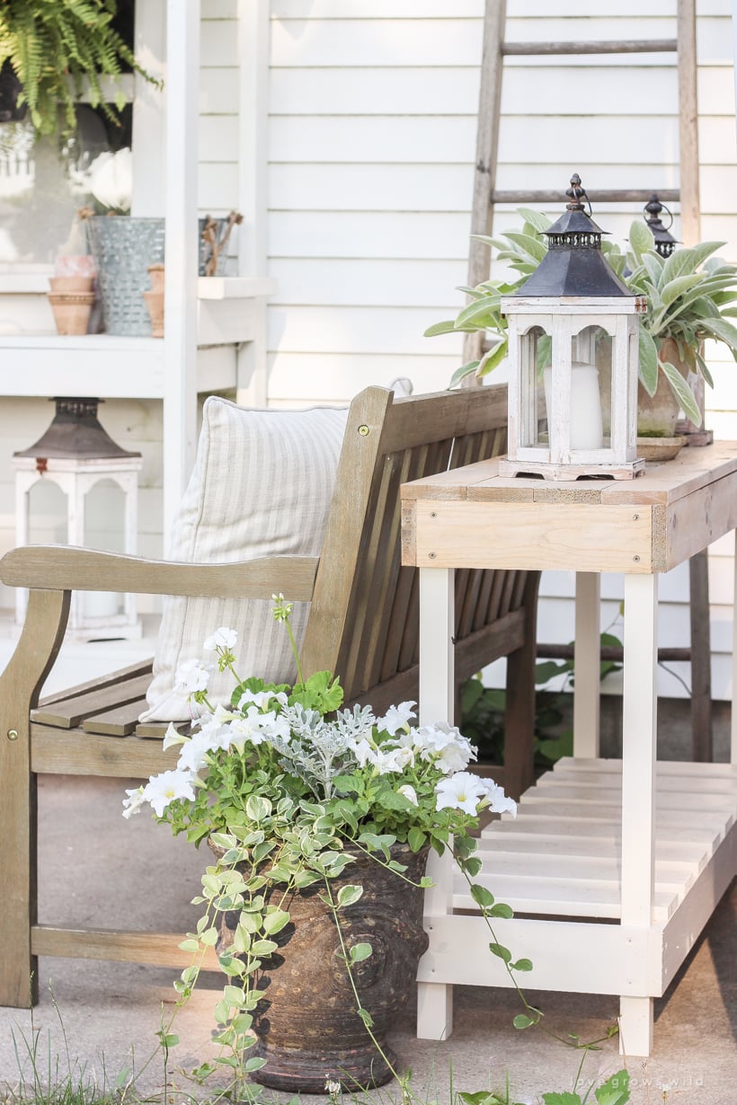 Outdoor Console Table | DIY Patio Furniture Idea White outdoor console table with a slatted lower shelf on a porch beside a wood bench, styled with a lantern and plants