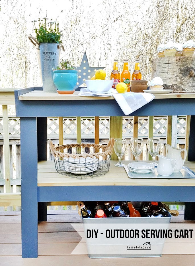Outdoor Serving Cart | DIY Patio Furniture Idea Blue painted wood outdoor serving cart on a deck holding lemons, sodas and a flower bucket, with plates on the lower shelf