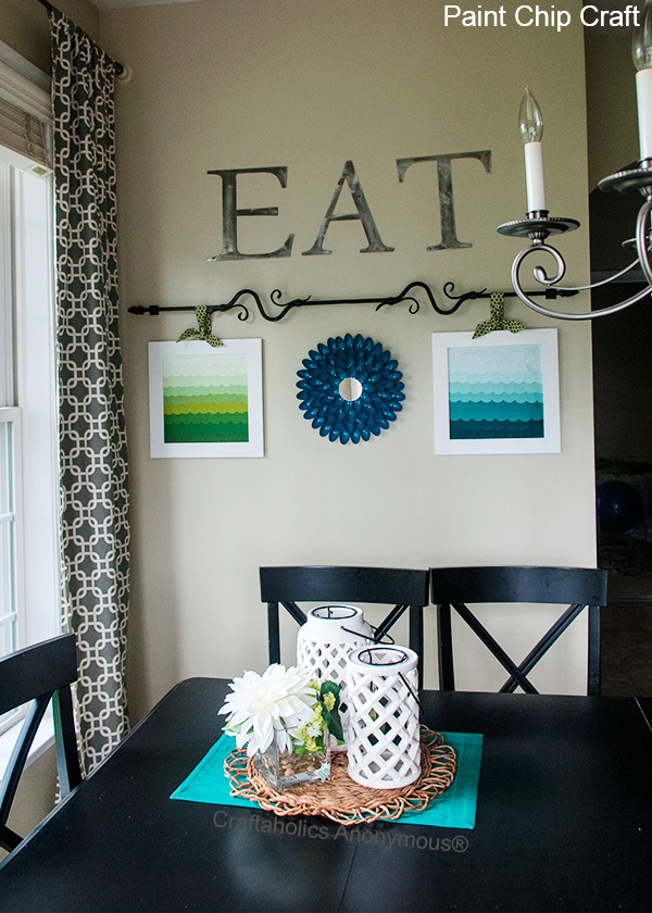 Paint chip art with ombre, overlapping circles in aqua to deep teal scallop rows inside a white square frame beside flowers
