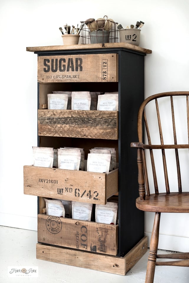 Black dresser with rustic reclaimed wood drawer fronts stenciled like vintage sugar crates, holding bags of milk paint