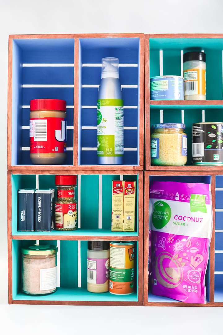 Stacked wood crates with stained outsides and blue and teal painted insides holding cans, jars and pantry items