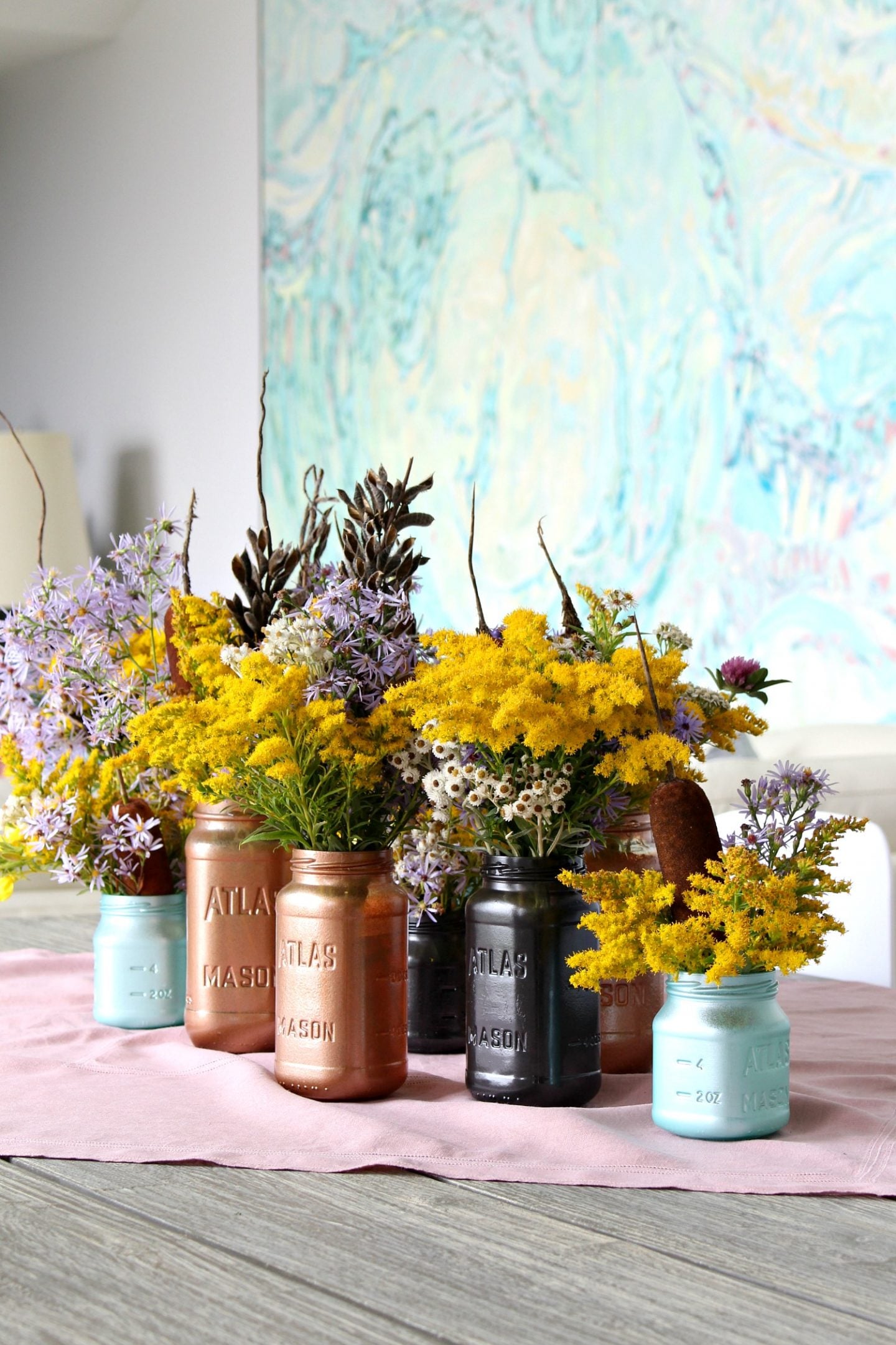 Spray painted mason jar vases in copper, sea mist and charcoal holding a wildflower centerpiece on a dining table