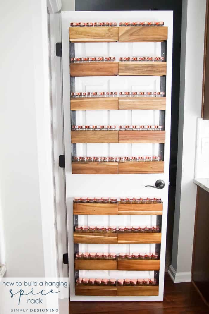 White pantry door lined top to bottom with wood plank spice racks on metal frames holding rows of copper lid jars