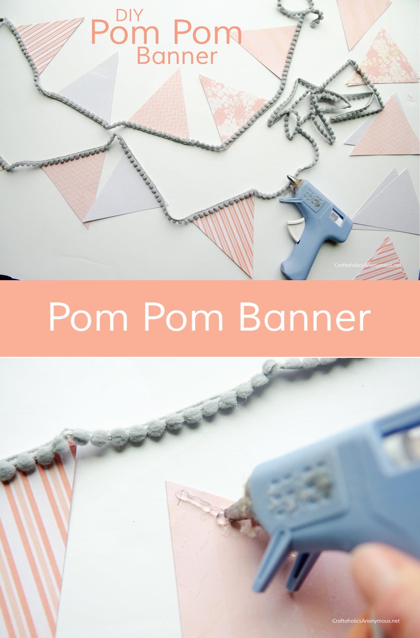 Paper pennant banner in pink and gray patterned triangles on mini gray pom pom trim beside a blue hot glue gun