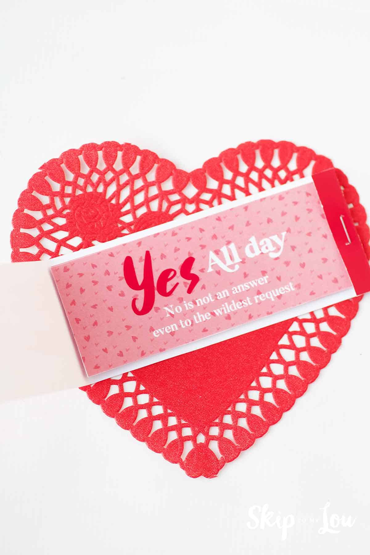Pink love coupon reading Yes All Day tucked into a red paper heart doily