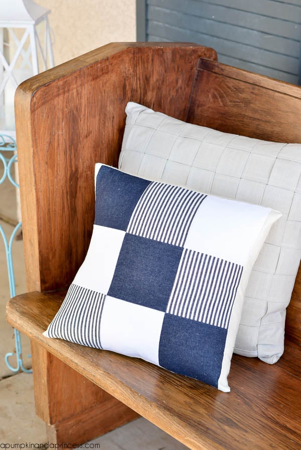 Patchwork pillow in navy denim, striped denim and white squares on a wood church pew in front of a woven gray pillow
