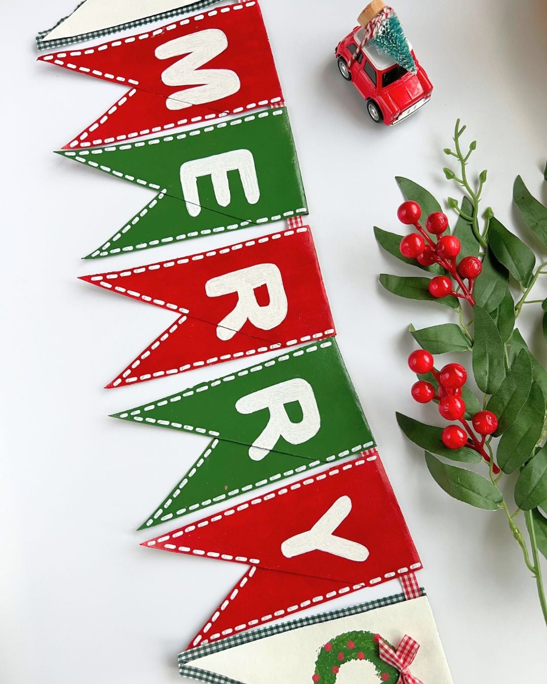 Recycled cardboard Christmas decor: a toilet paper roll Christmas banner hung on a wall with red and green letter pennants