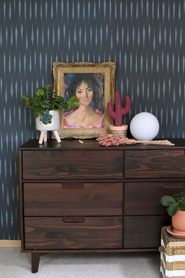 Navy and white removable wallpaper accent wall behind a walnut dresser with a gold framed portrait and plants