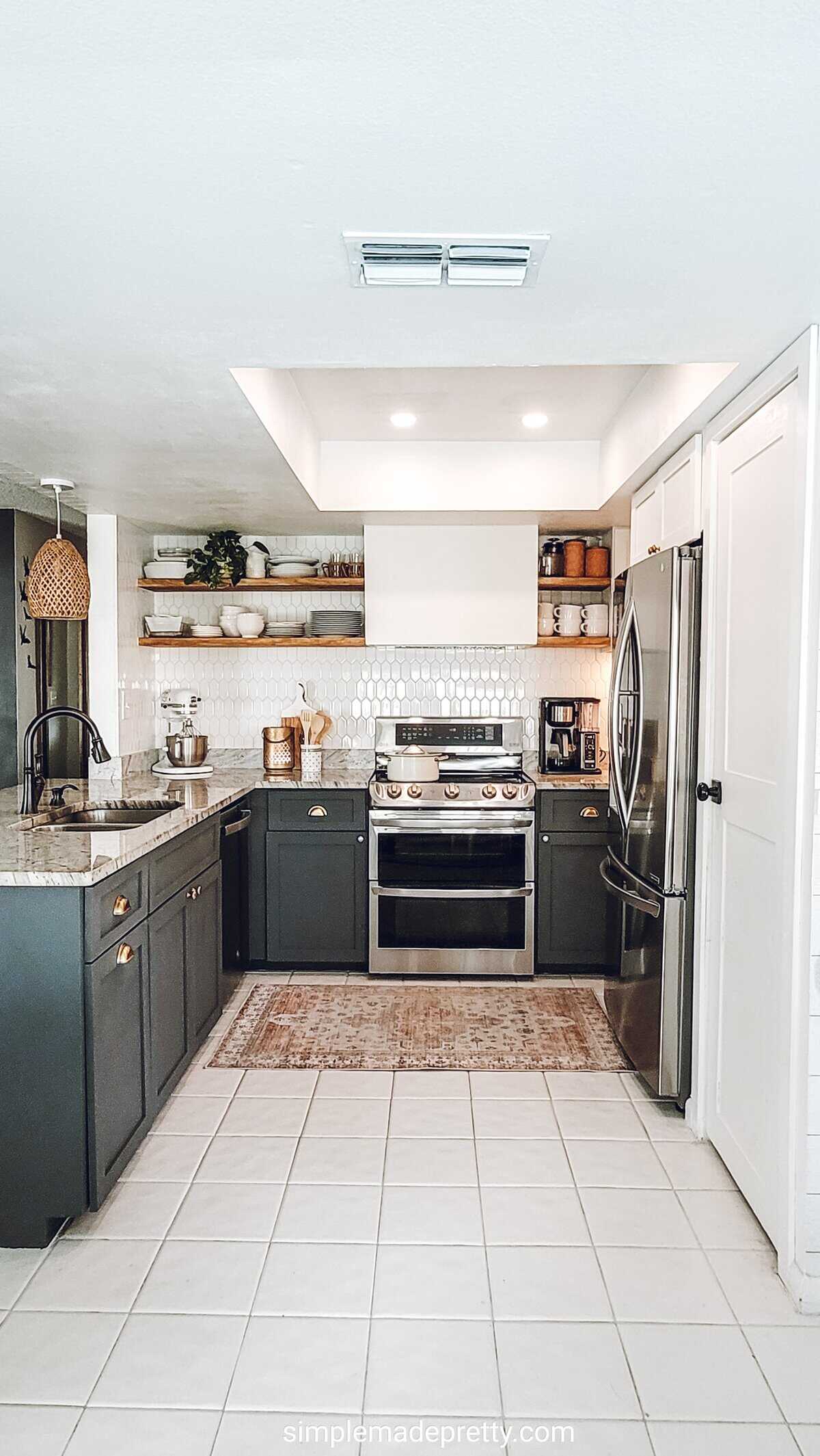 Kitchen with dark green base cabinets, gold cup pulls, wood open shelves, a white hood and tile floor