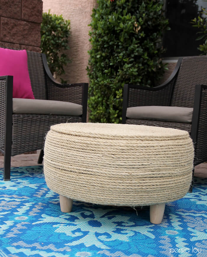 Round tire coffee table wrapped in natural sisal rope on short wood feet, sitting on a blue patterned rug on a patio