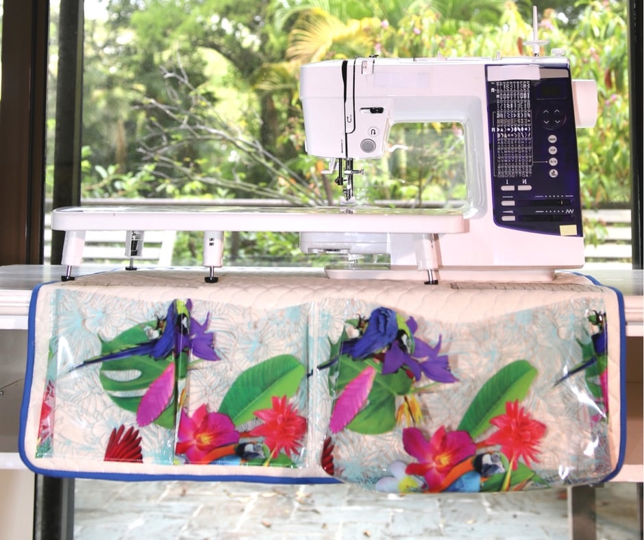 Quilted sewing mat with clear vinyl pockets in a bright tropical flower print, hanging under the front of a sewing machine