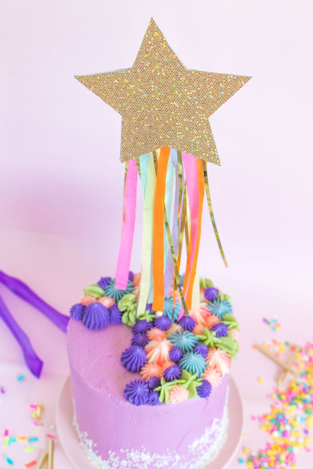 Shooting Star Cake Topper | DIY Party Decorations Idea Glittery gold star cake topper with colorful tissue paper and tinsel streamers on a purple frosted cake