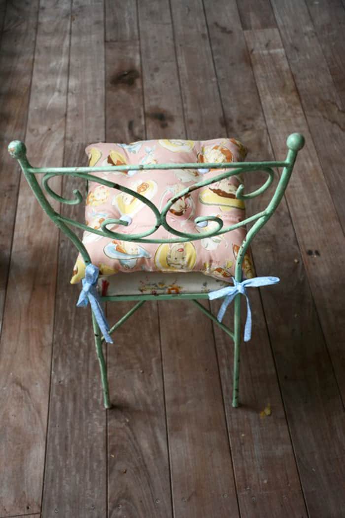 Simple Tie-On Chair Cushion | Home Sewing Project Tie-on chair cushion in a pink vintage floral print tied with blue fabric ties onto a green iron chair on wood floors