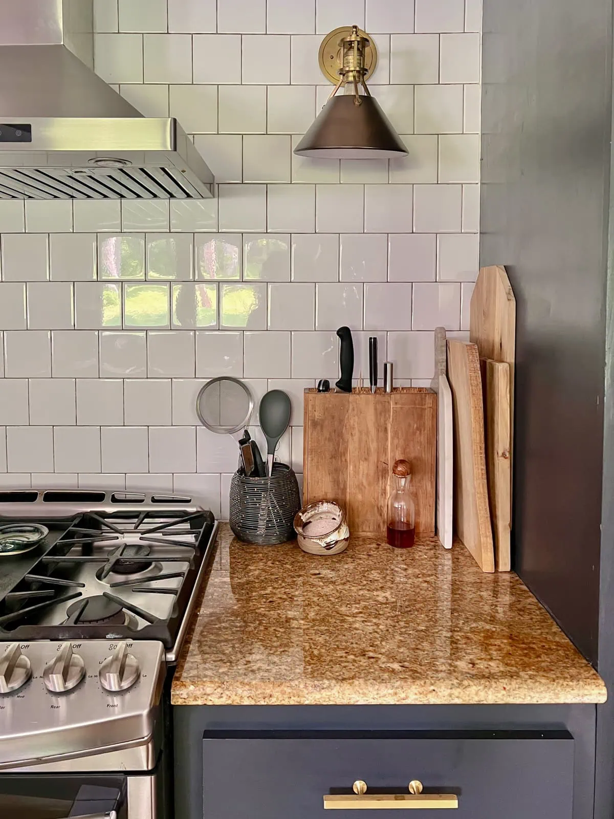 Stained wood knife block with knives standing in it on a granite counter beside cutting boards and a white tile wall