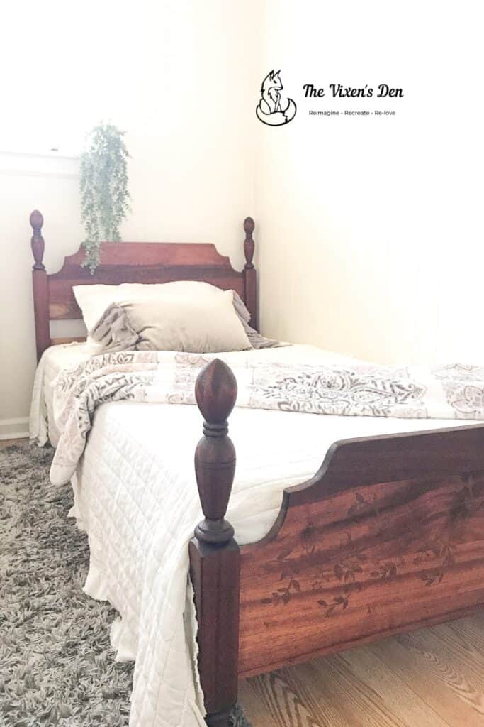 Sanded mahogany twin headboard and footboard with a stained vine stencil, made up with white bedding beside a gray rug