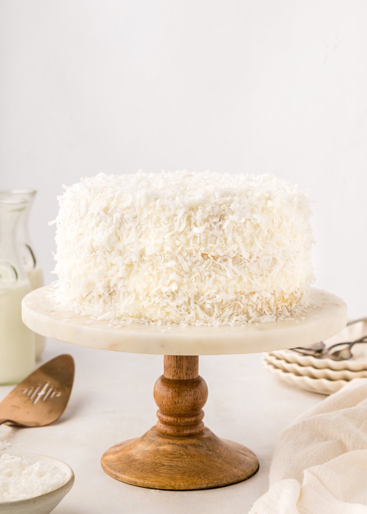 Three layer coconut birthday cake covered in shredded coconut on a white marble cake stand