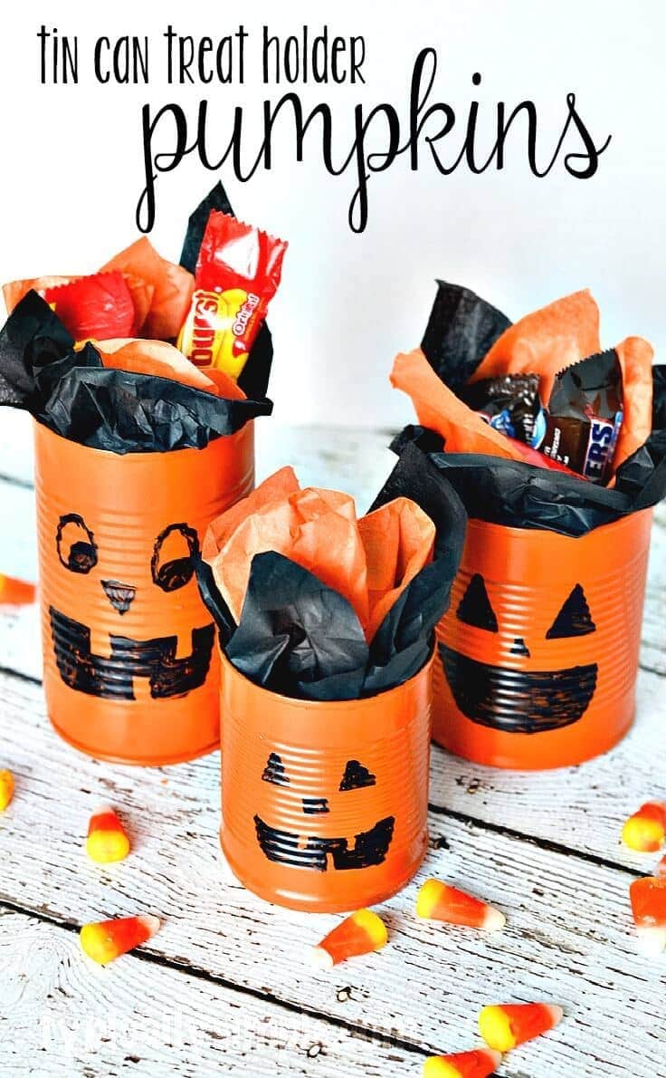 Orange painted tin can jack o'lantern treat holders with black marker faces, stuffed with tissue paper and candy