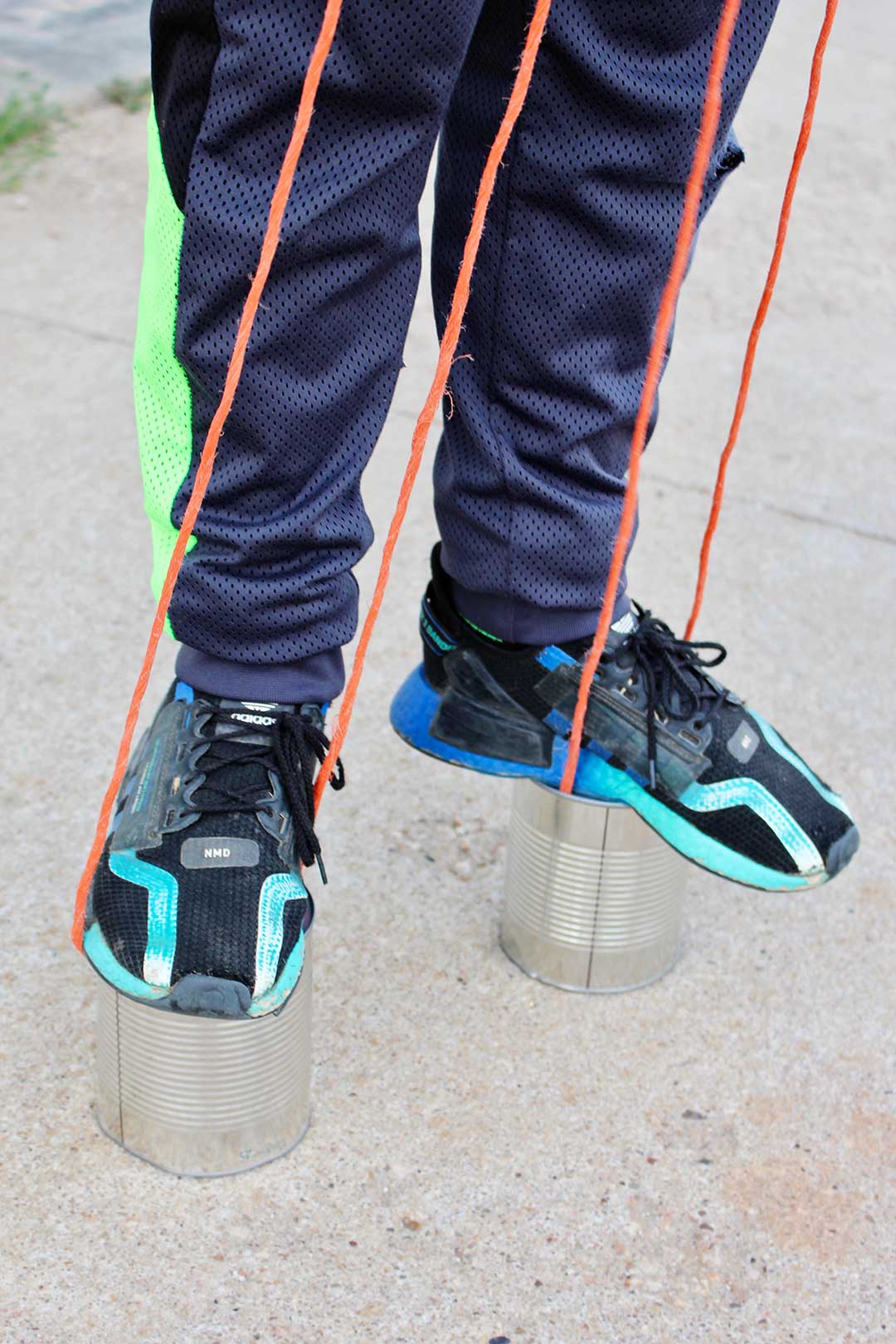 Child standing and balancing on homemade tin can stilts made from large fruit cans, holding on to long rope handles