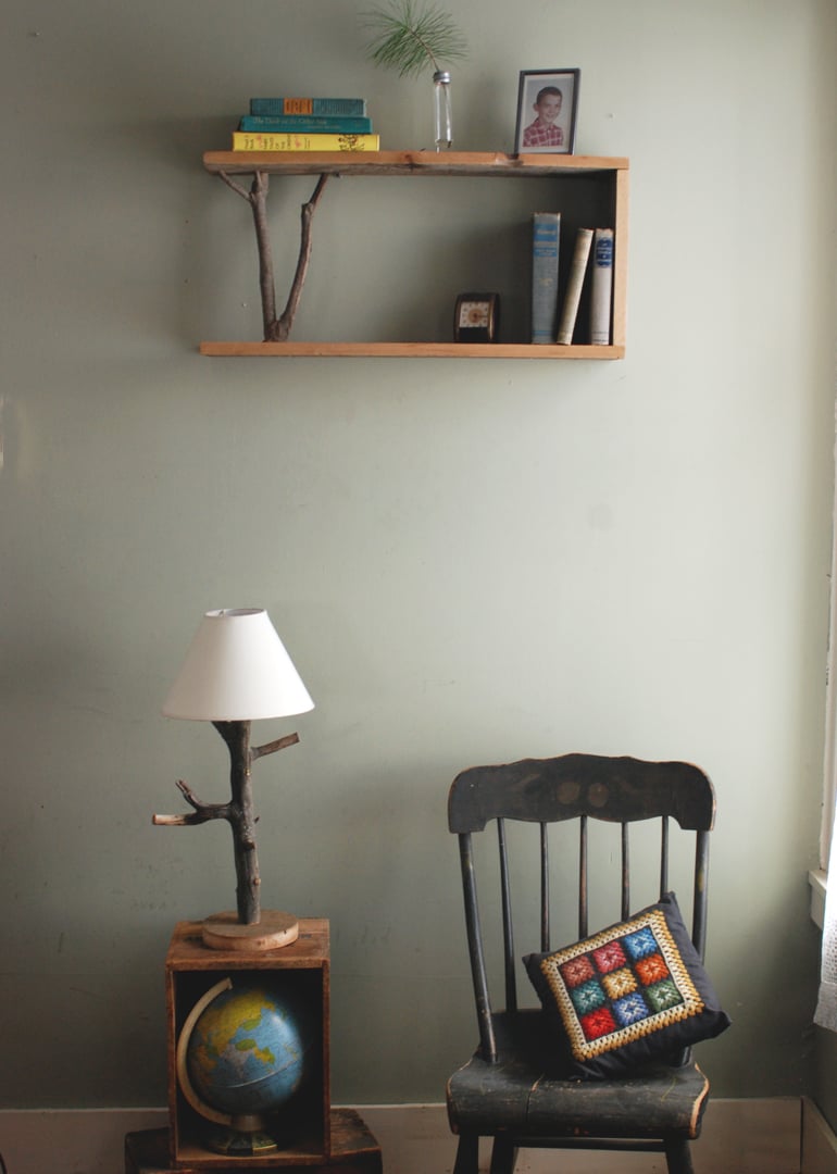Table lamp with a natural tree branch base and white shade on a wood crate holding a globe, next to an old wooden chair