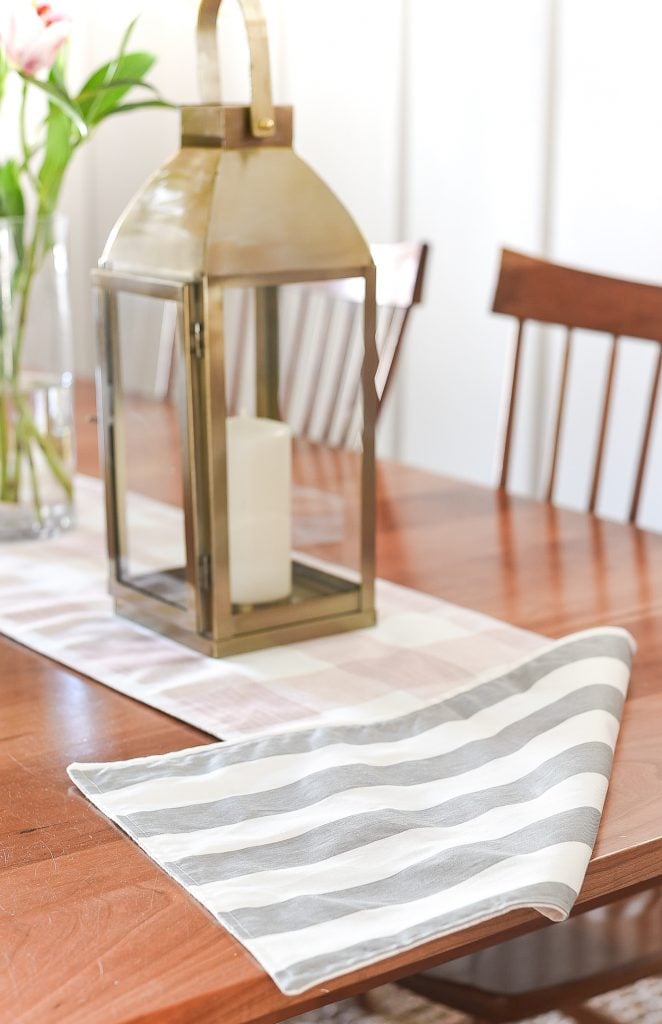 Two-Sided Table Runner | Home Sewing Project Reversible table runner with gray and white stripes under a brass lantern and candle on a wood dining table set with chairs