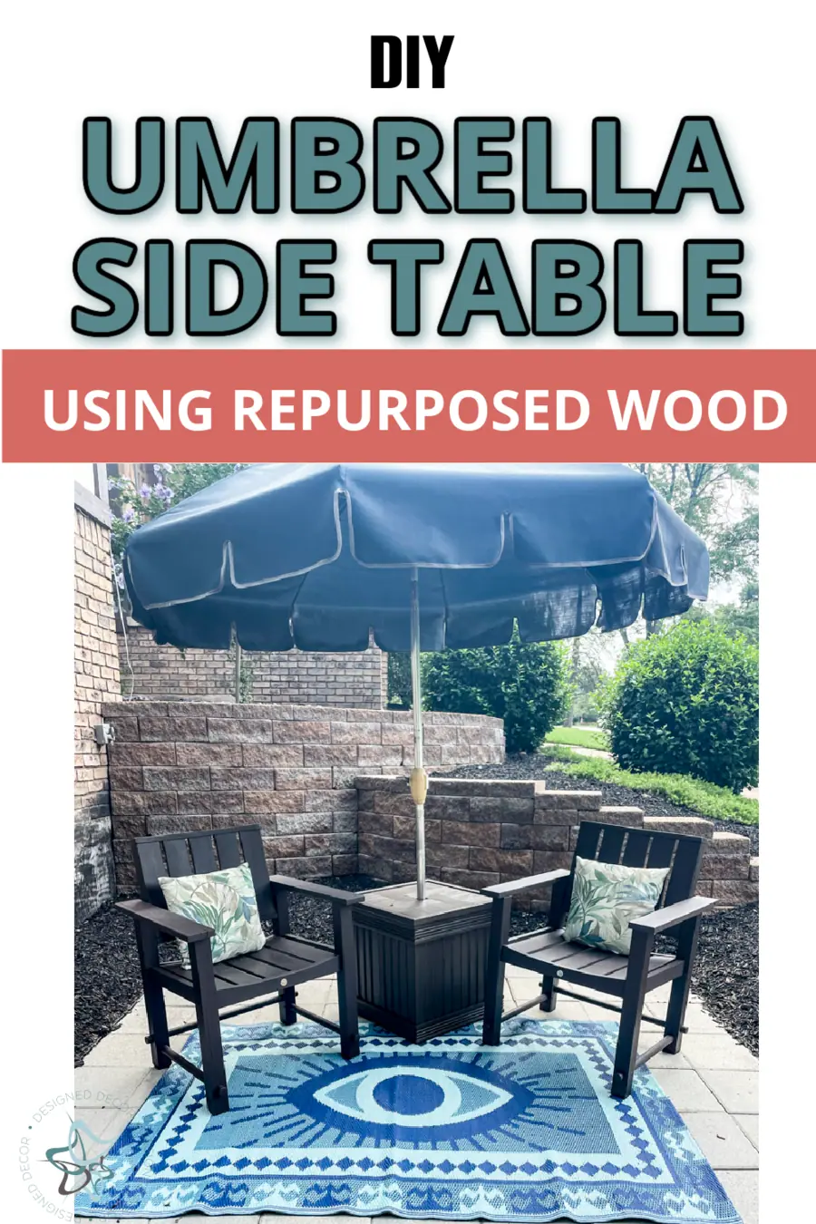 Umbrella Side Table | DIY Patio Furniture Idea Umbrella side table made from repurposed wood between two black patio chairs under a blue umbrella on a bright rug