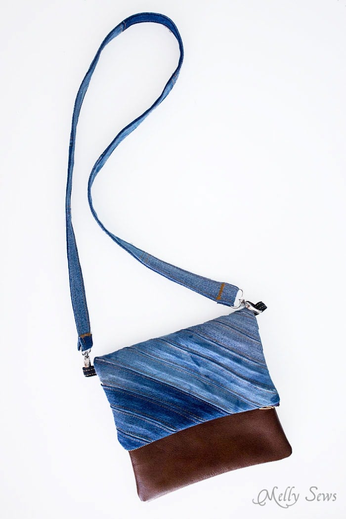 Fold-over clutch with diagonal stripes of mixed denim, a brown faux leather bottom and a long denim crossbody strap