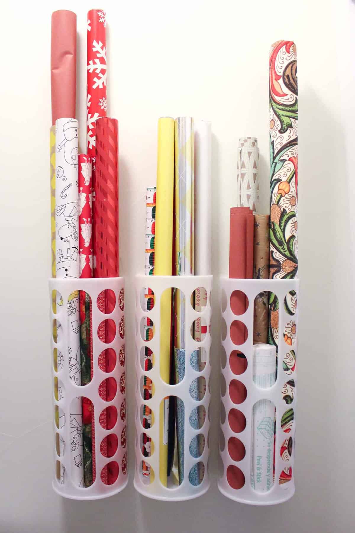 Rolls of red, yellow and patterned wrapping paper standing upright in three white IKEA plastic dispensers on a wall